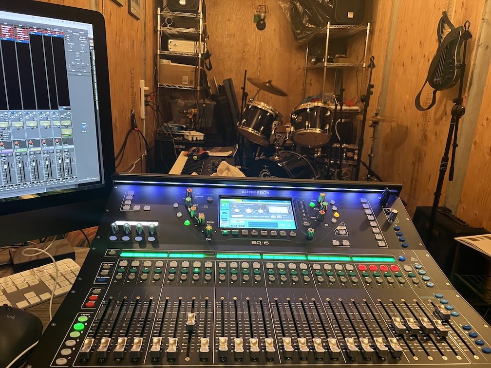 Mixing board, drums, and other instruments in a wooden-walled rehearsal room.